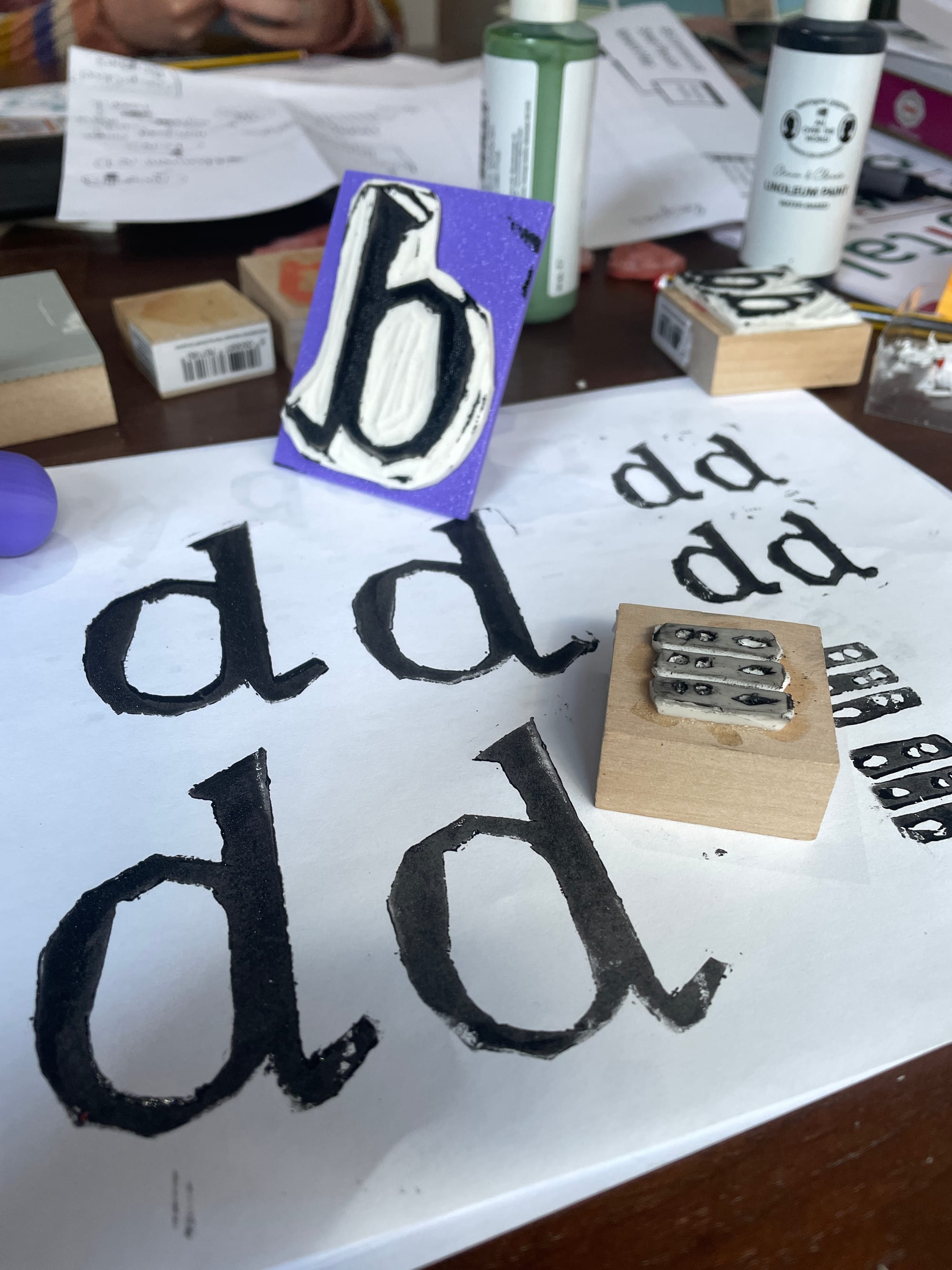 lino cut print blocks, and black ink prints of the letters dd on white paper