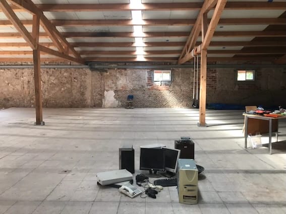 Photo of a warehouse space with a small collection of computers and montors in the foreground, and a desk and chair in the background.